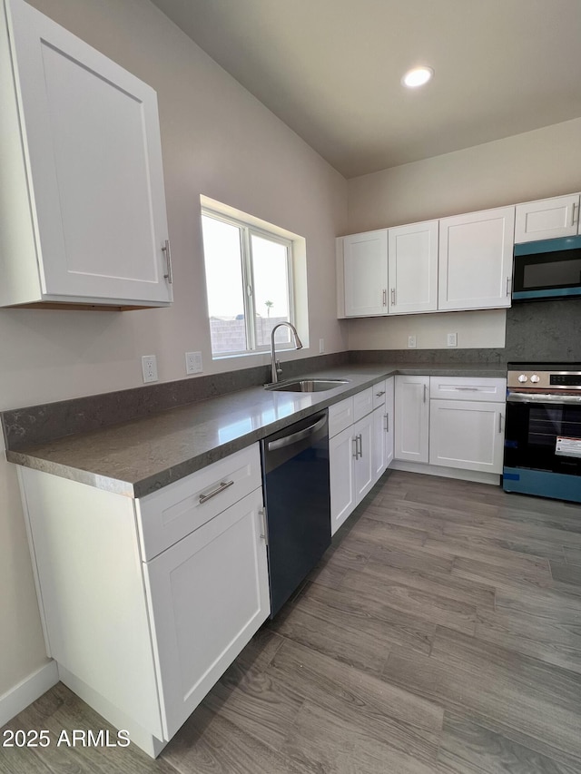 kitchen with stainless steel appliances, dark countertops, white cabinets, a sink, and wood finished floors