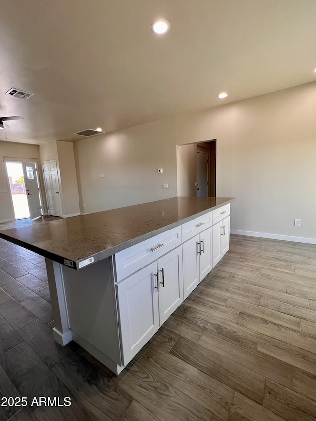 kitchen with white cabinets, visible vents, a kitchen island, and wood finished floors