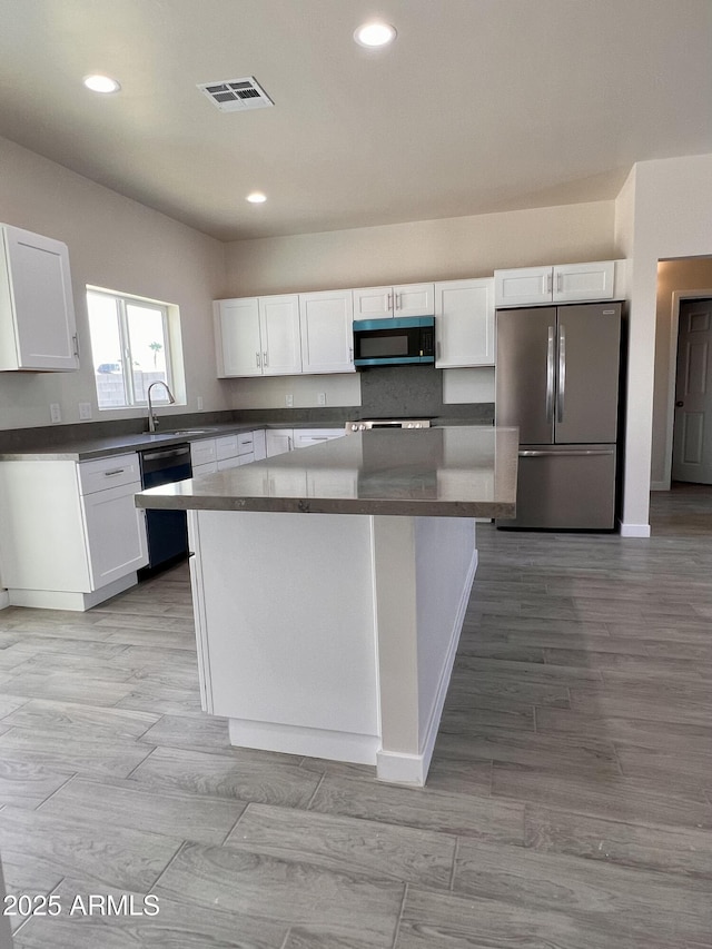 kitchen featuring stainless steel appliances, dark countertops, visible vents, white cabinetry, and a kitchen island