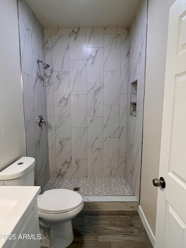 full bath featuring toilet, a tile shower, vanity, wood finished floors, and baseboards