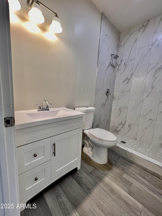 full bathroom with tiled shower, vanity, toilet, and wood finished floors