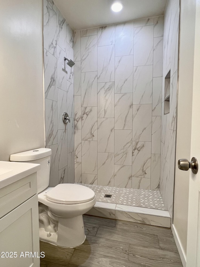 bathroom featuring vanity, a tile shower, and toilet