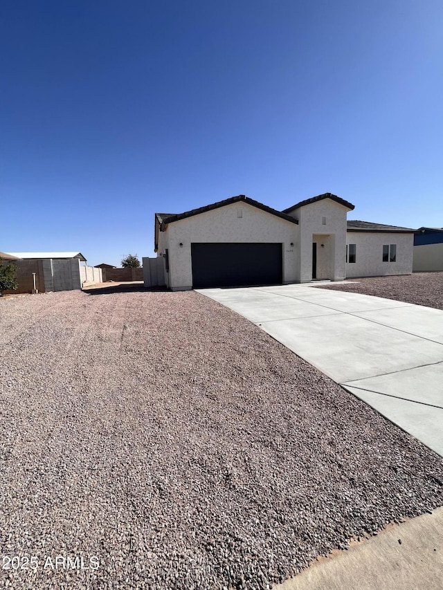 view of front facade featuring an attached garage, driveway, fence, and stucco siding