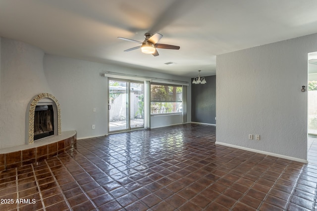 unfurnished living room featuring visible vents, a textured wall, baseboards, a fireplace with raised hearth, and ceiling fan with notable chandelier