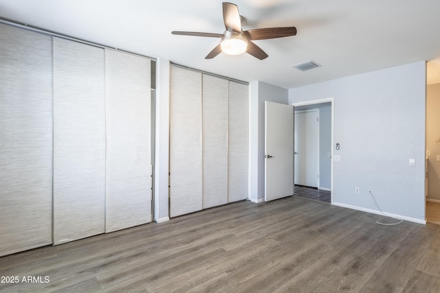 unfurnished bedroom with ceiling fan, multiple closets, baseboards, wood finished floors, and visible vents