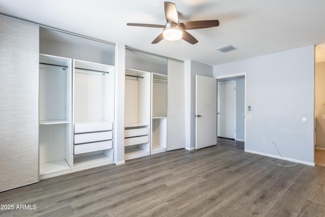 unfurnished bedroom featuring a ceiling fan, two closets, wood finished floors, and visible vents