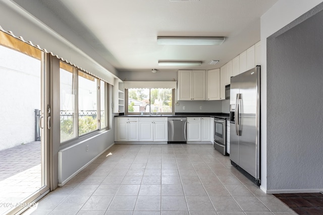 kitchen featuring dark countertops, a sink, light tile patterned floors, white cabinets, and stainless steel appliances