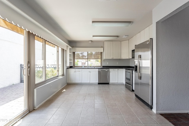kitchen with dark countertops, white cabinetry, a sink, appliances with stainless steel finishes, and light tile patterned floors