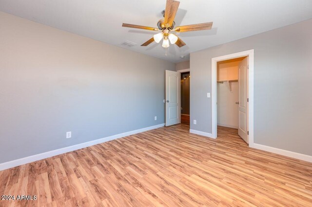 unfurnished bedroom featuring ceiling fan, light wood-type flooring, a closet, and a walk in closet