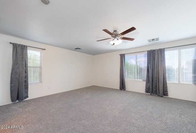 carpeted spare room featuring ceiling fan and plenty of natural light