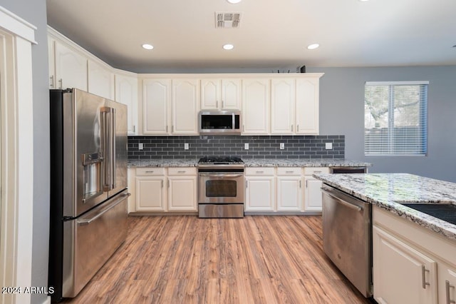 kitchen featuring tasteful backsplash, appliances with stainless steel finishes, light hardwood / wood-style flooring, and light stone counters