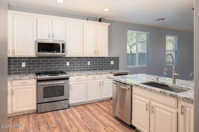 kitchen with light stone countertops, sink, light hardwood / wood-style flooring, appliances with stainless steel finishes, and backsplash