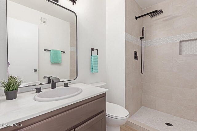 bathroom featuring a tile shower, vanity, and toilet