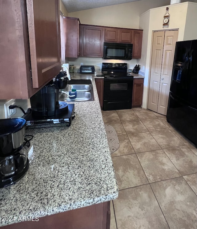 kitchen featuring vaulted ceiling, light stone countertops, light tile patterned floors, black appliances, and sink