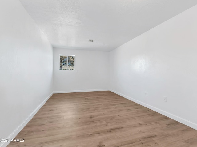 spare room featuring baseboards, a textured ceiling, visible vents, and light wood-style floors