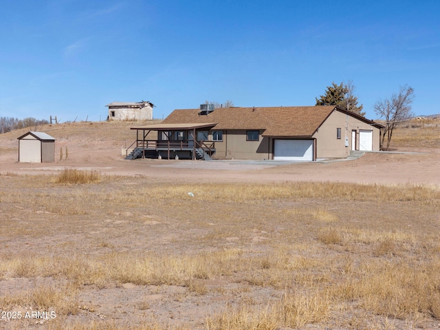 back of house with a rural view, central AC, a detached garage, and a storage unit