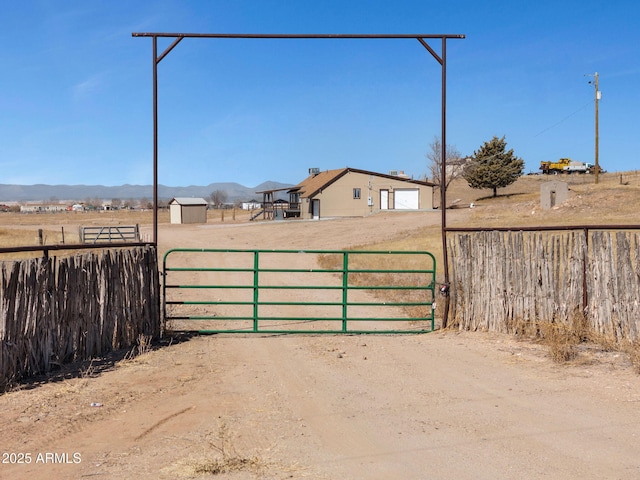 view of gate with a storage unit, a rural view, an outdoor structure, and fence