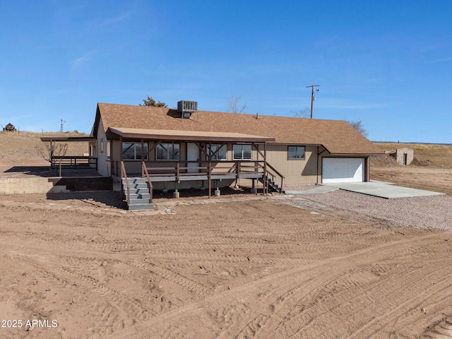 view of front of property featuring driveway, a garage, central AC unit, and roof with shingles