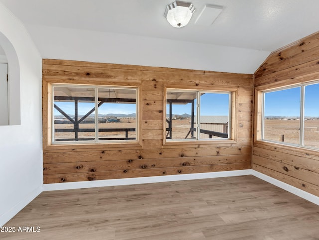 empty room featuring vaulted ceiling, wooden walls, baseboards, and wood finished floors