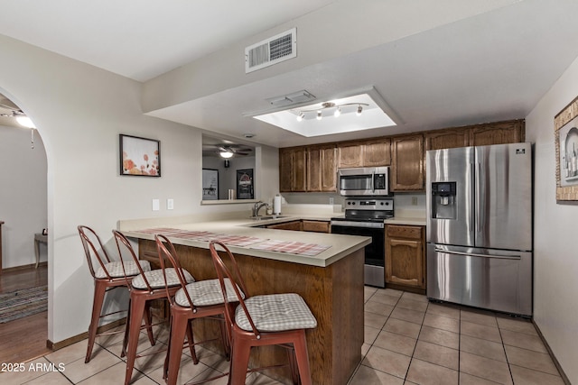 kitchen featuring sink, appliances with stainless steel finishes, light tile patterned flooring, a kitchen bar, and kitchen peninsula