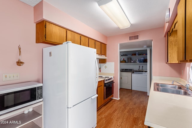 kitchen featuring light hardwood / wood-style floors, white appliances, sink, washing machine and dryer, and a textured ceiling