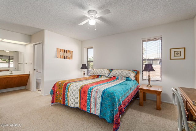 bedroom featuring ceiling fan, light colored carpet, a textured ceiling, and ensuite bath