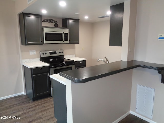 kitchen featuring dark wood finished floors, a peninsula, visible vents, and appliances with stainless steel finishes