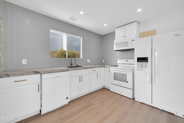 kitchen featuring light wood-type flooring, visible vents, a sink, white appliances, and decorative backsplash