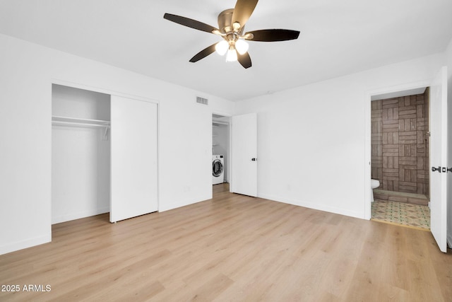 unfurnished bedroom with wood finished floors, baseboards, a closet, ensuite bathroom, and washing machine and dryer