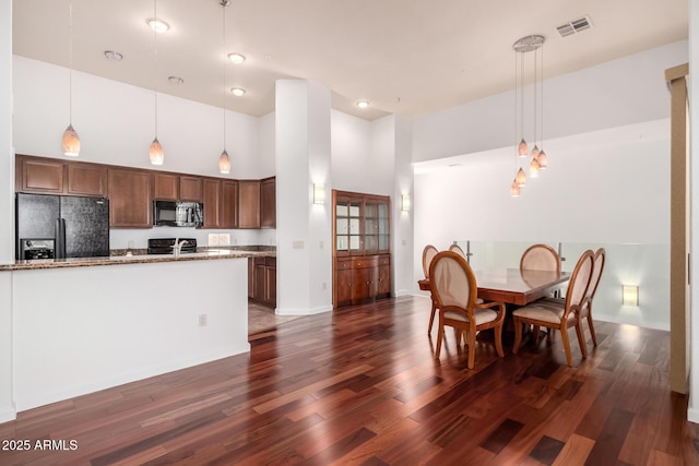 20801 N 90th Pl Unit 210, Scottsdale, AZ 85255 - kitchen with visible vents, a towering ceiling, light stone countertops, black appliances, and dark wood-type flooring