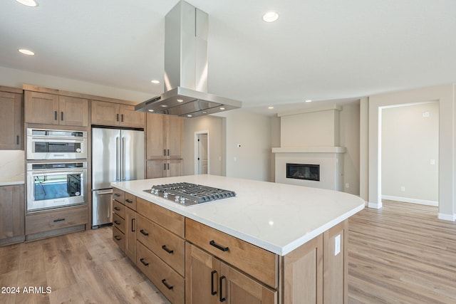 kitchen featuring stainless steel appliances, wall chimney range hood, light stone counters, light hardwood / wood-style flooring, and a kitchen island