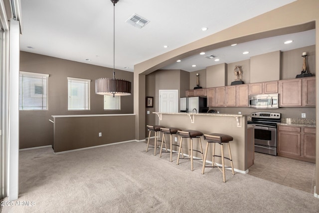 kitchen featuring decorative light fixtures, light colored carpet, stainless steel appliances, and a breakfast bar area