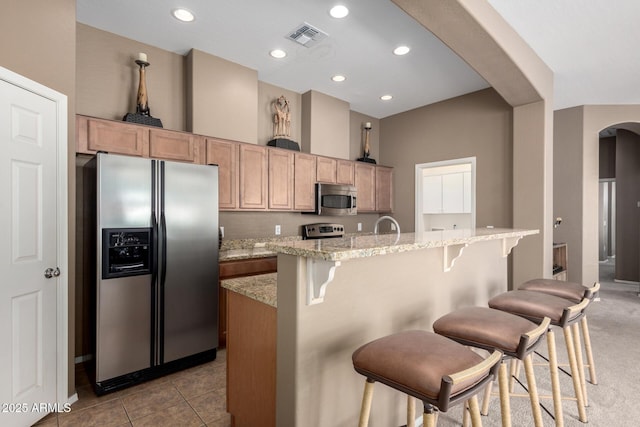 kitchen with a breakfast bar, light stone counters, a kitchen island with sink, and appliances with stainless steel finishes