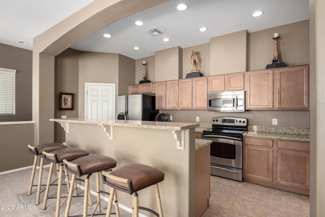 kitchen with a kitchen bar, stainless steel appliances, light stone counters, and a kitchen island with sink