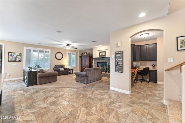 living room featuring a fireplace, built in study area, stone finish flooring, and baseboards