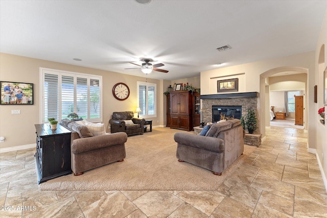 living area featuring visible vents, stone tile flooring, arched walkways, a fireplace, and baseboards