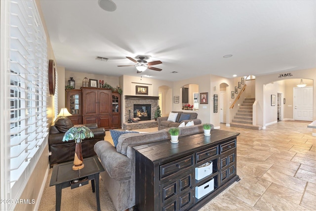 living room featuring visible vents, stairs, stone tile flooring, a fireplace, and arched walkways