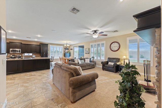 living area featuring ceiling fan with notable chandelier, a healthy amount of sunlight, visible vents, and baseboards