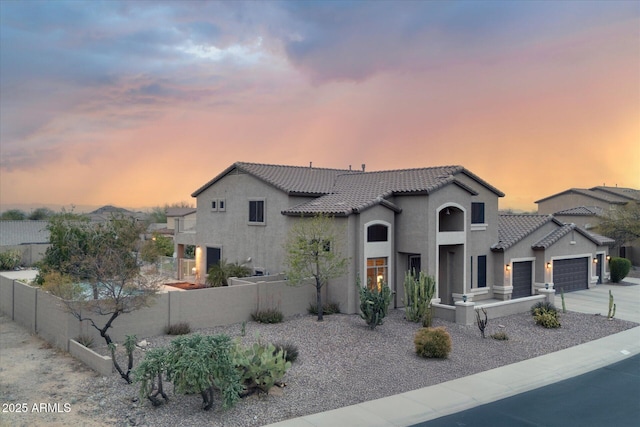 mediterranean / spanish-style house with stucco siding, driveway, a tile roof, fence, and an attached garage