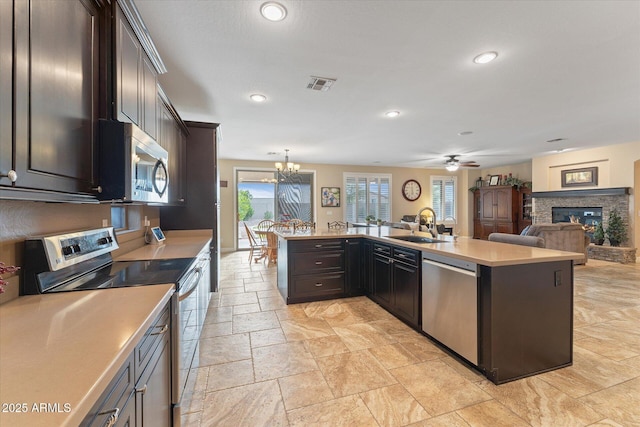 kitchen with visible vents, a sink, a stone fireplace, light countertops, and stainless steel appliances