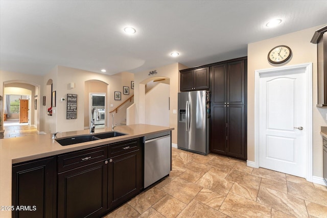 kitchen with a sink, arched walkways, appliances with stainless steel finishes, and light countertops