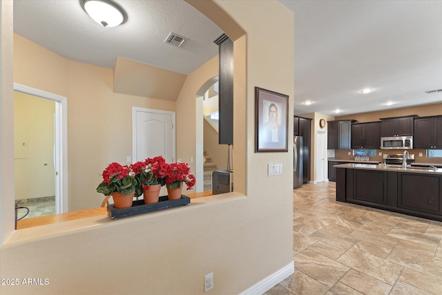 kitchen featuring visible vents, stainless steel appliances, arched walkways, light countertops, and dark brown cabinets