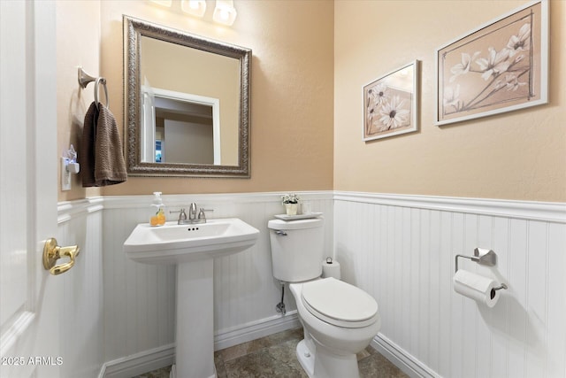 half bath with a sink, toilet, and wainscoting