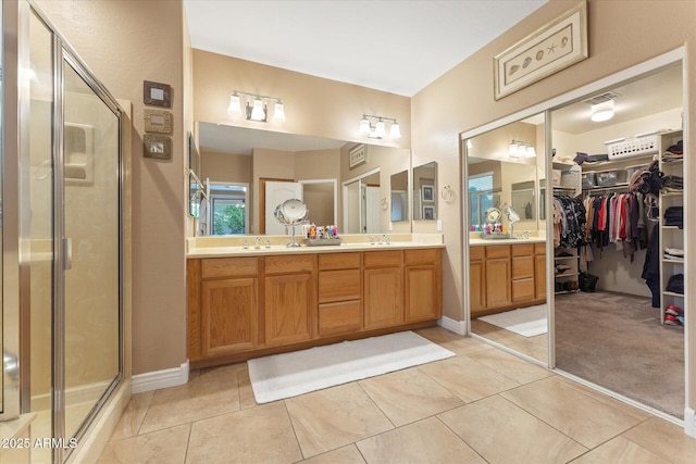 full bathroom featuring double vanity, a sink, a shower stall, a walk in closet, and tile patterned floors