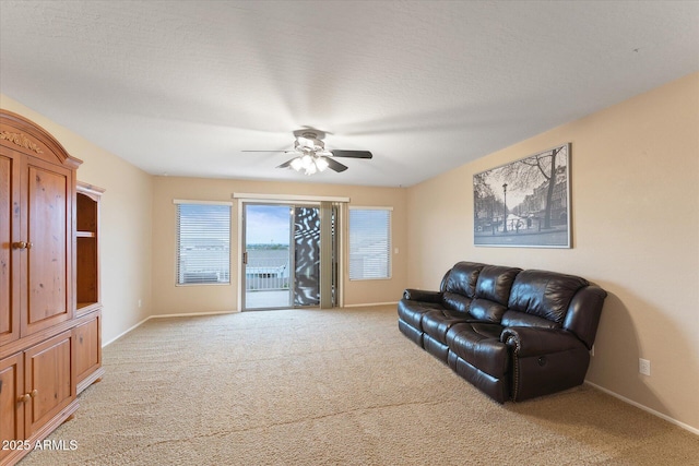 living room featuring light colored carpet, a textured ceiling, a ceiling fan, and baseboards