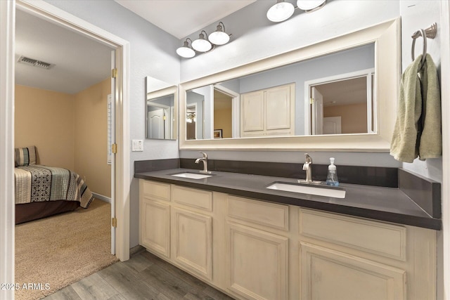 ensuite bathroom featuring double vanity, wood finished floors, visible vents, and a sink