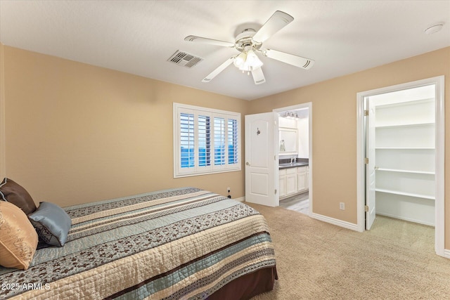 bedroom with a spacious closet, visible vents, baseboards, light colored carpet, and a ceiling fan