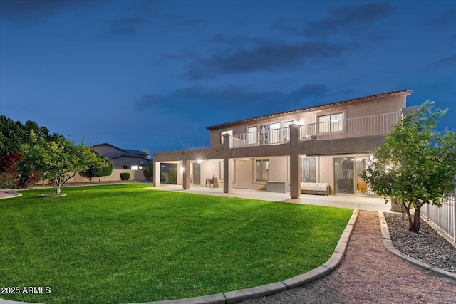 back of property featuring a balcony, a fenced backyard, stucco siding, a patio area, and a lawn