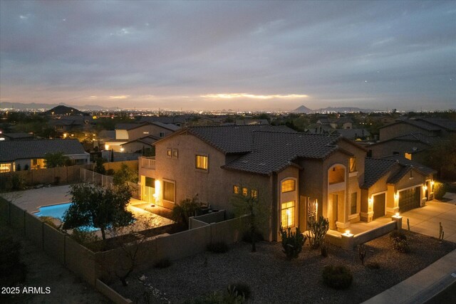 view of front of house with stucco siding, driveway, a fenced backyard, a garage, and a fenced in pool