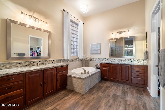 bathroom with wood-type flooring, a bath, decorative backsplash, and vanity